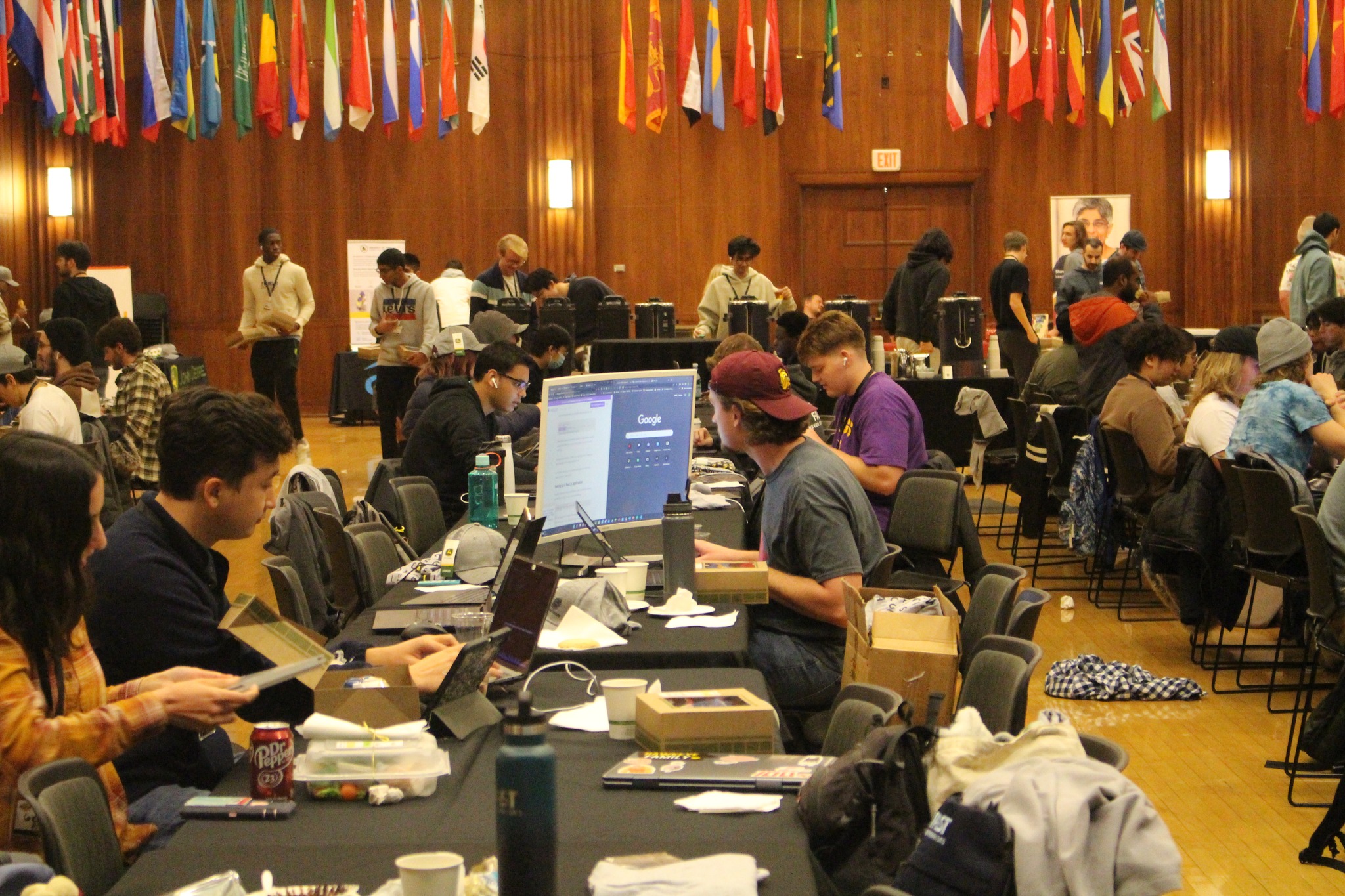 A room full of people sitting at tables and staring at computers and monitors